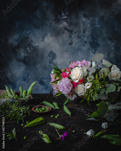 still life with assorted flowers, fresh green pea in a brown plate on a wooden table, toned for a vintage effect