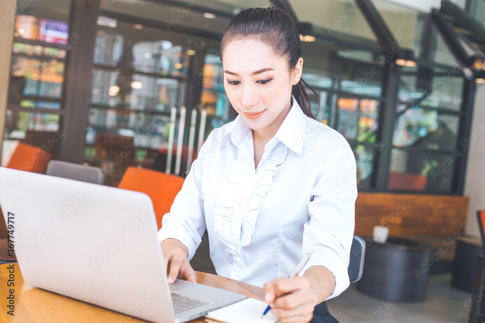 Business woman working in a computer and writing with a pen at a notepad in the office. Business woman working in a computer and writing with a pen at a notepad in the office.