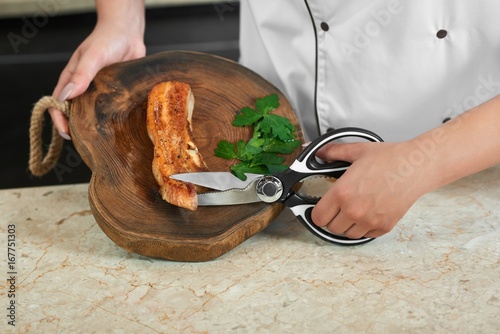Cropped close up of a female chef cutting grilled meat with scissors working at the restaurant kitchen. photo