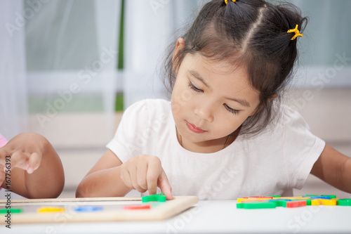 Cute little child girl having fun to play and learn magnetic alphabets on board in the room