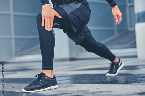 Sporty male is stretching his legs outdoors.