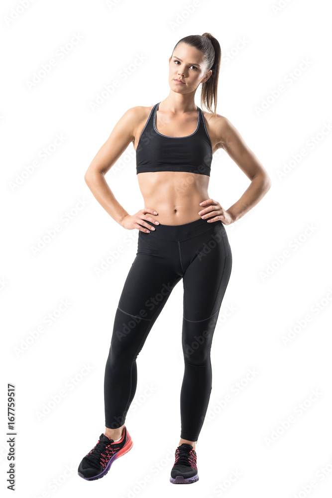 Fitness young pretty woman in black leggings and tank top posing with hands on hips. Full body length portrait isolated on white studio background Fitness young pretty woman in black leggings and tank top posing with hands on hips. Full body length portrait isolated on white studio background