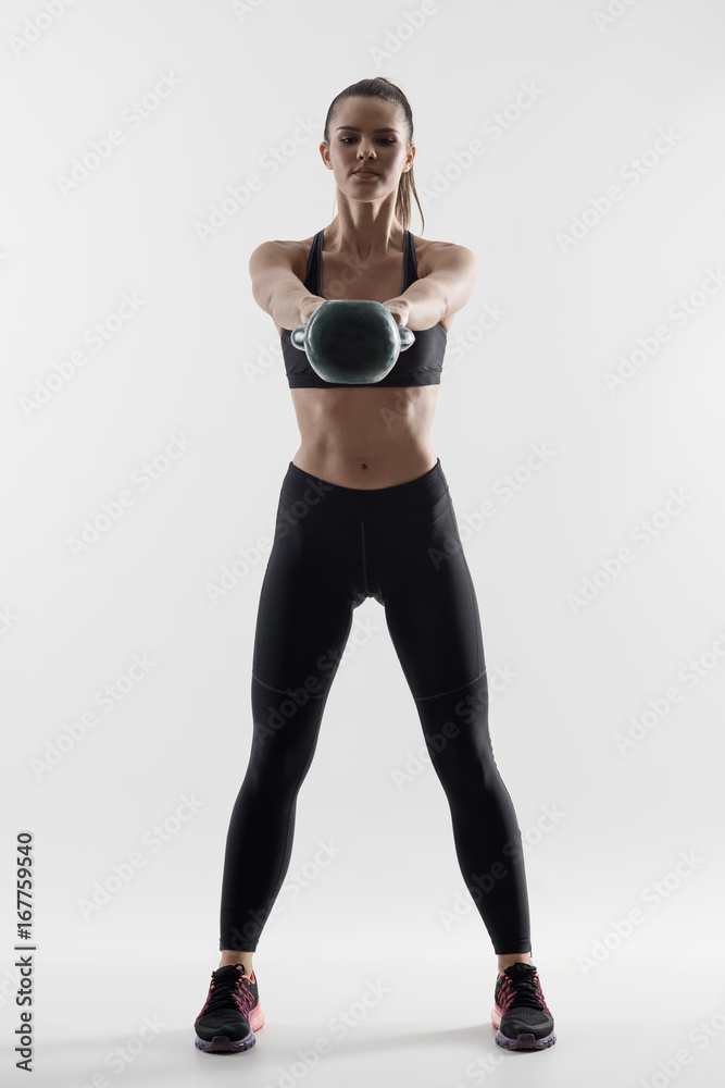 Front view back lit silhouette of strong fit woman doing kettlebell swing training exercise. Desaturated full body portrait on gray background.