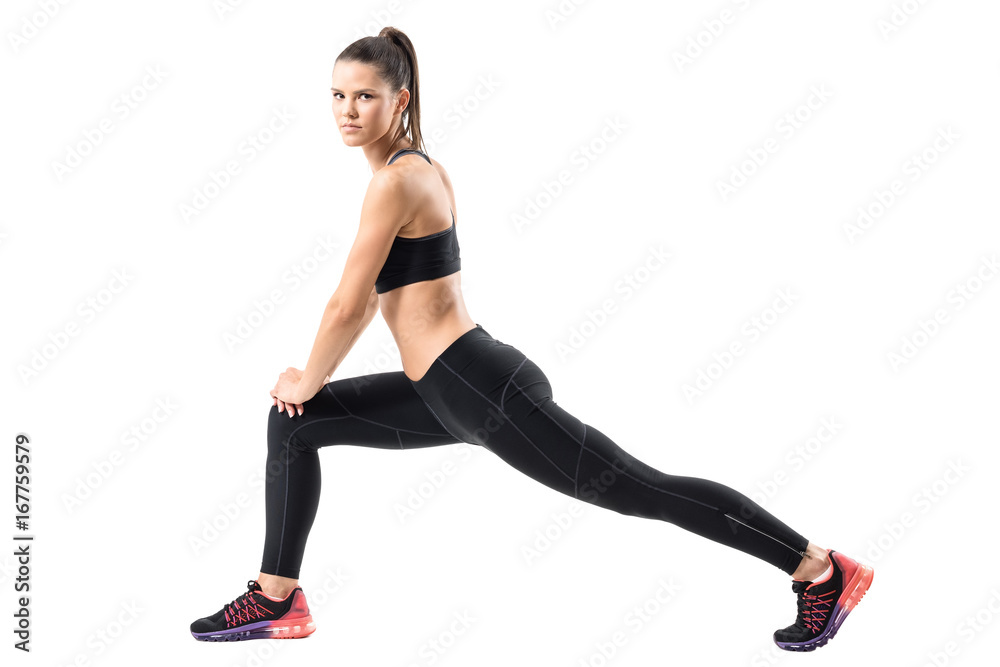 Side view of young female in sportswear doing forward lunge exercise. Full body length portrait isolated on white studio background