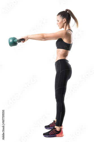 Side view of strong sporty fitness woman swinging 12 kg kettlebell in mid air motion. Full body length portrait isolated on white studio background © sharplaninac