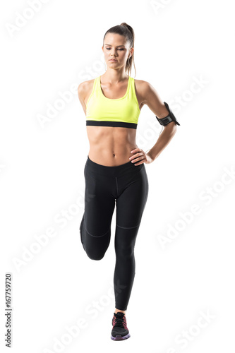 Front view of athletic young pretty woman jogger stretching leg muscles exercise. Full body length portrait isolated on white studio background