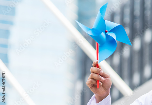 Portrait of hand with wind turbine paper, save energy concept, city background.
