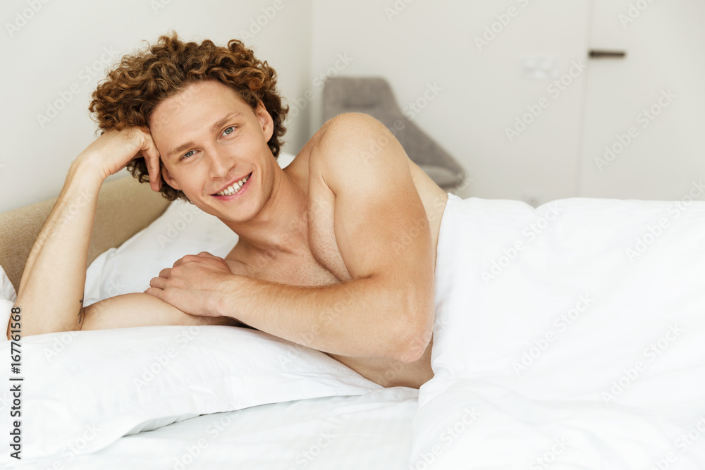 Handsome young man lying in bed and looking at camera Handsome young man lying in bed and looking at camera