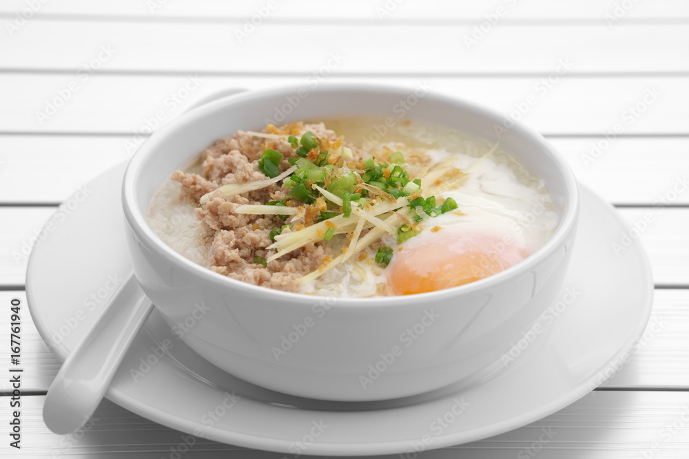 pork chops rice porridge or congee with soft boiled egg and vegetable in the white bowl with spoon on the aluminium table for delicious breakfast and clean food in the morning