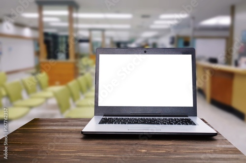 Laptop notebook computer with white blank screen on wooden desk with blurred view of empty chairs in clinic or hospital, heart health care and medical technology concept, selective focus, copy space