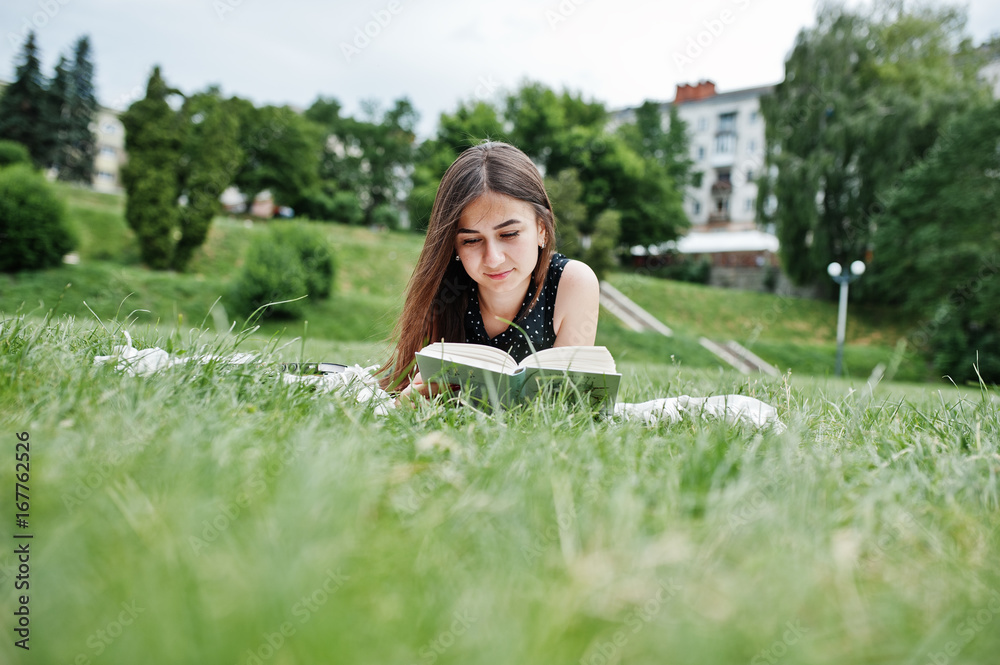 Portrait of a beautiful woman in black polka dot dress laying on the blanket on the grass and reading. Portrait of a beautiful woman in black polka dot dress laying on the blanket on the grass and reading.