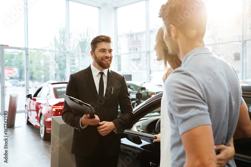 Smiling salesman showing new car to a couple