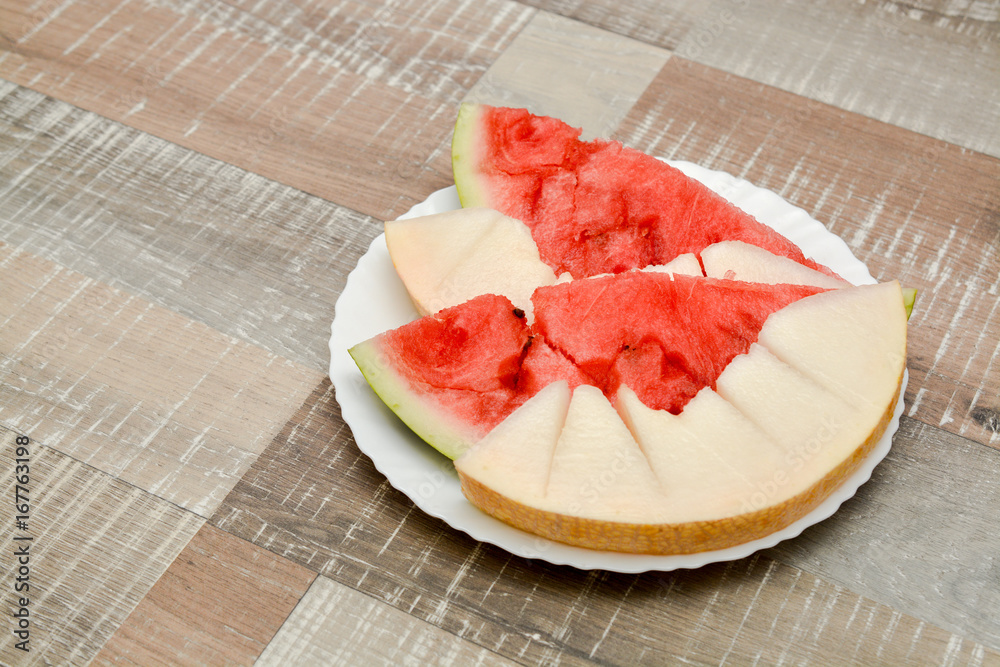 Slices of watermelon and melon in a plate on a wooden table. Summer fruit