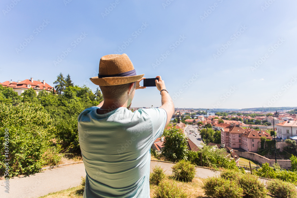 Back view of a young man tourist taking photo with smartphone in front of city