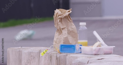 prepackaged brown bag school lunch outside with plastic bag passing in background - environmental impact photo