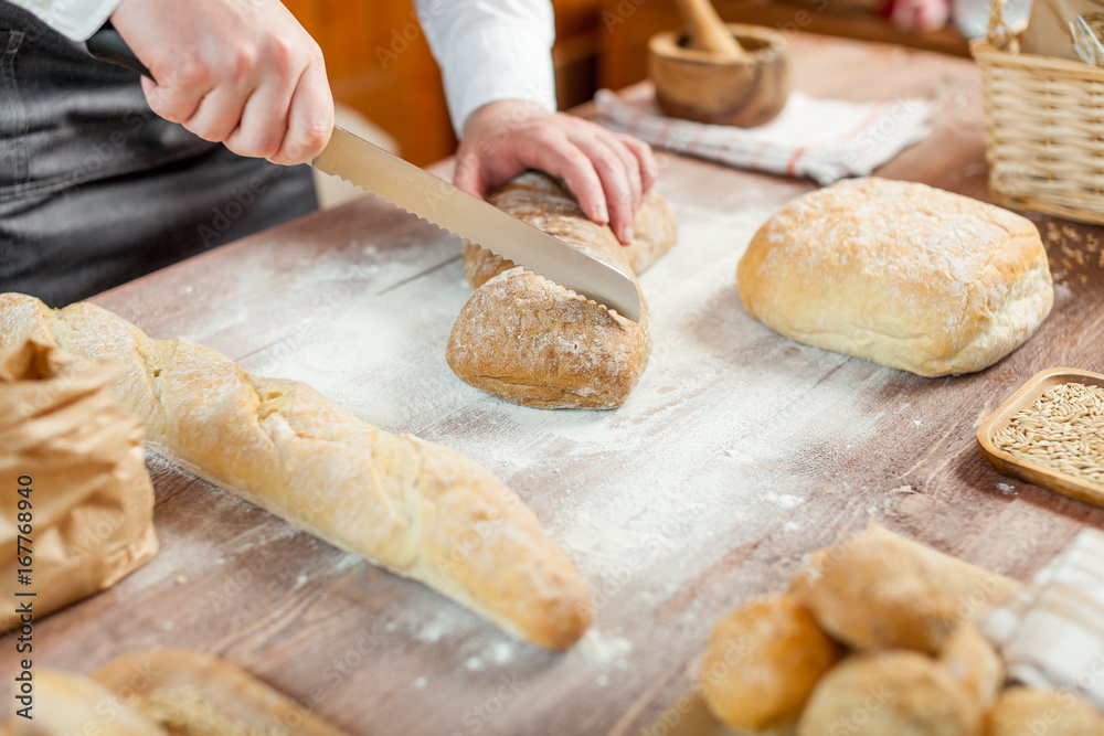 Male hands cutting fresh bread on the wooden table, selective focus