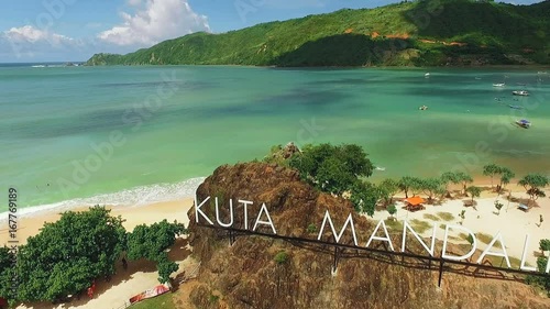 Aerial view of Kuta Mandalika beach sign letters with white sand and turquoise water surrounded by green hills. Shot with drone on sunny day with blue sky in Lombok, Indonesia, fly forward. photo