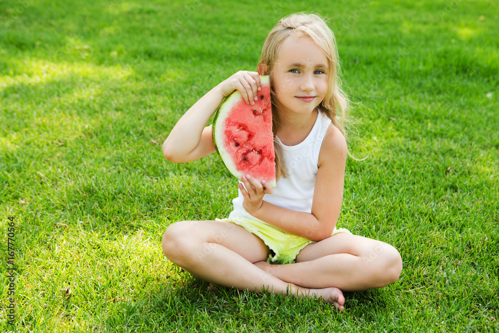 Happy little girl eating watermelon on the grass in summertime Happy little girl eating watermelon on the grass in summertime