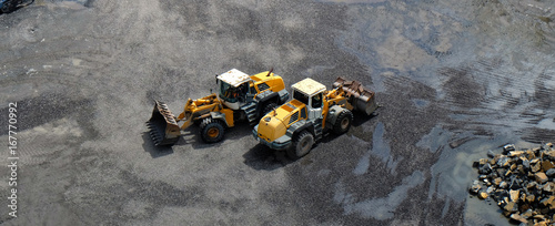 Two wheel loader vehicles with front buckets passing each other, crossing in opposite directions during earth moving works in a construction site, mine or stone pit / quarry © Lightstone