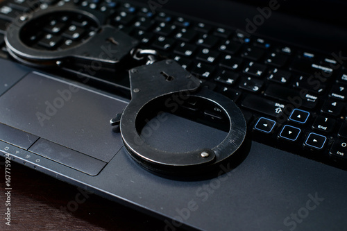 steel police handcuffs lying on keyboard. Concept of internet crime, hacking, cyber crimes and virtual payments