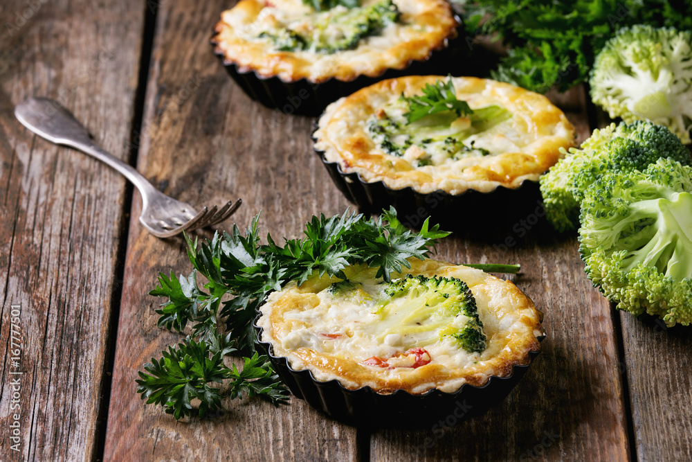 Baked homemade quiche pie in mini metal forms served with fresh greens and fork on old plank wooden background. Close up with space Baked homemade quiche pie in mini metal forms served with fresh greens and fork on old plank wooden background. Close up with space
