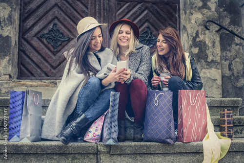 Three best friends enjoying after shopping. Young girls sitting on the stairs and reading text messages.