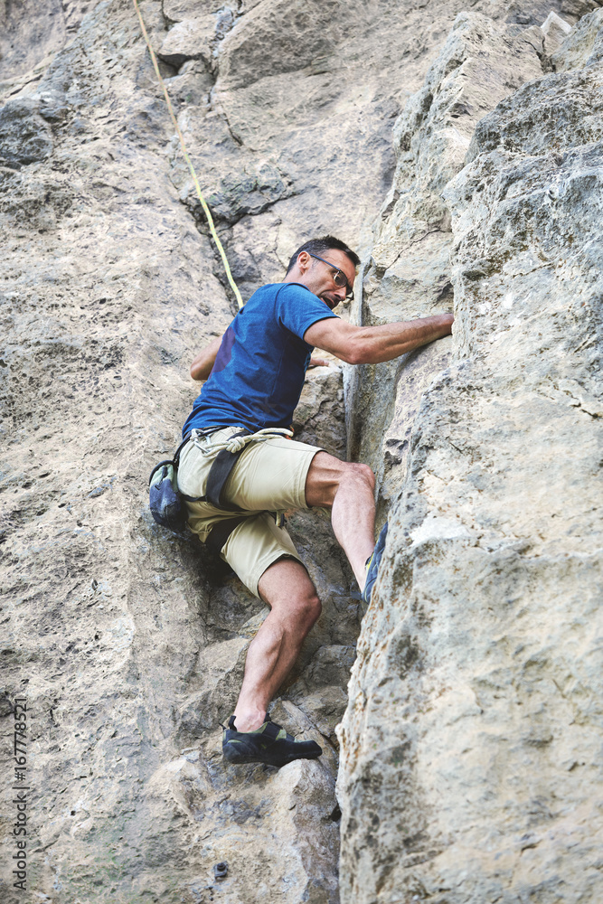 adult man rock climber. rock climber climbs on a rocky wall. man makes hard move. bottom view