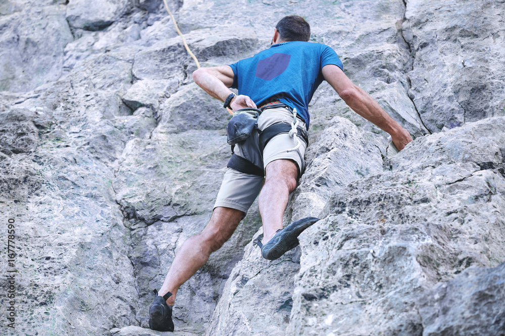 adult man rock climber. rock climber climbs on a rocky wall. man makes hard move. bottom view adult man rock climber. rock climber climbs on a rocky wall. man makes hard move. bottom view