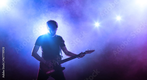 Silhouette of guitar player on stage on blue background with smoke and spotlights	