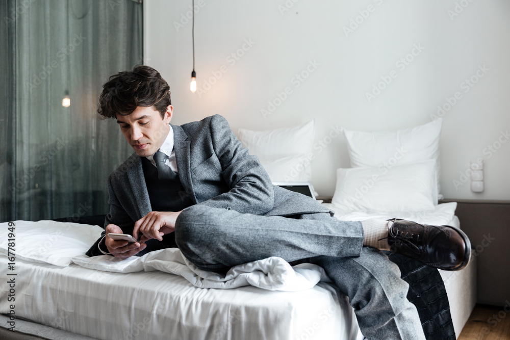 Businessman using smartphone while lying on a bed Businessman using smartphone while lying on a bed