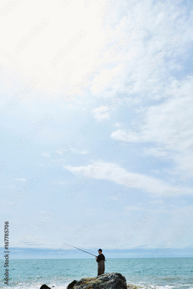 Distant view of young man standing on rock sea fishing Distant view of young man standing on rock sea fishing