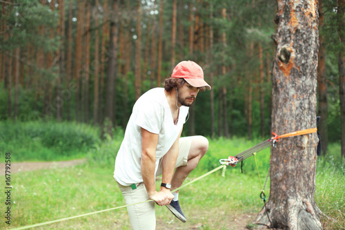 Sport, leisure - young man slacklining balancing on a rope in the forest