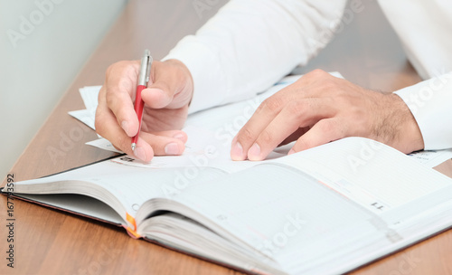 Unrecognizable businessman taking notes in dairy,