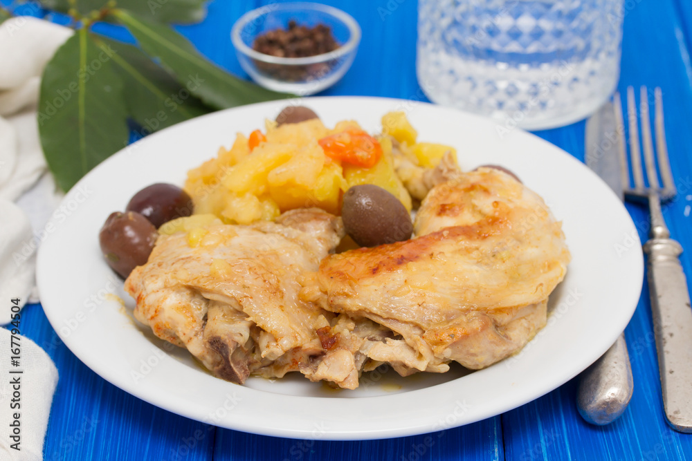 chicken with potato and olives on white plate on wooden background