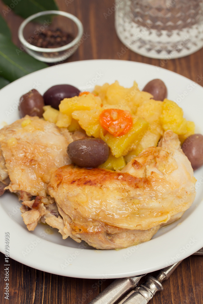 chicken with potato and olives on white plate on wooden background chicken with potato and olives on white plate on wooden background