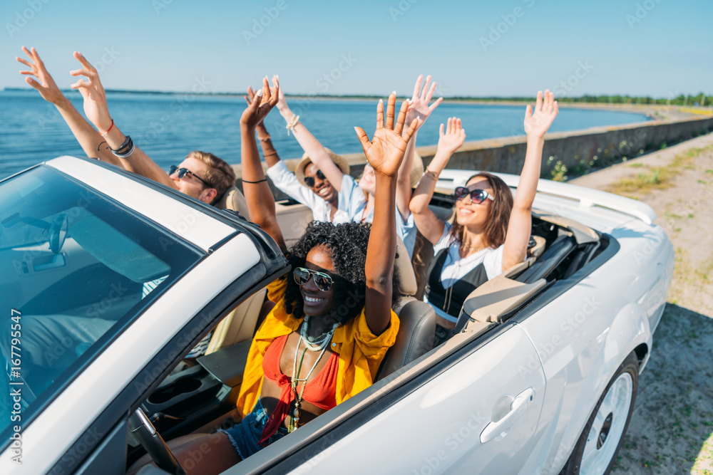 multiethnic smiling friends riding car while traveling together