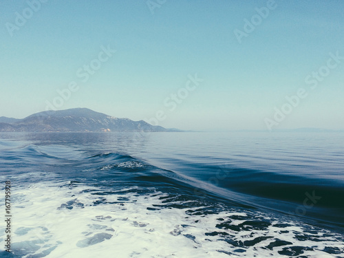 Sea view of Skiathos island. Waves on the sea left by the ship. Vibrant blue sea and sky. © diignat
