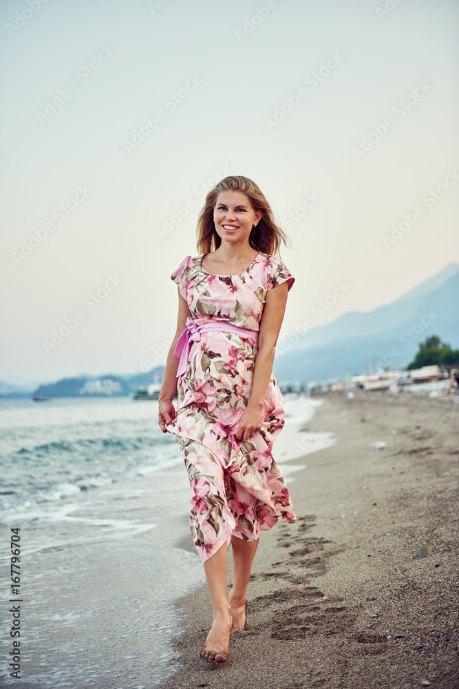 Young attractive woman in beautiful long dress stepping on seashore at sunset. Pregnancy and healthy lifestyle. Young attractive woman in beautiful long dress stepping on seashore at sunset. Pregnancy and healthy lifestyle.