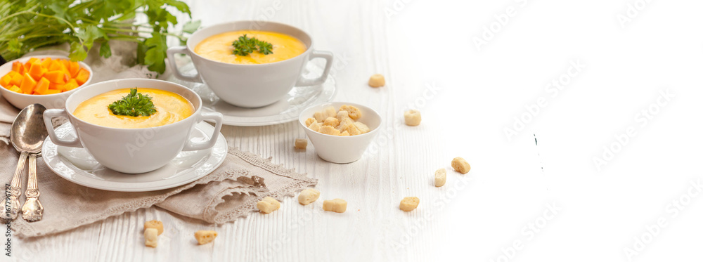 Pumpkin cream soup with croutons, raw fresh pumpkin pieces and herbs on a white rustic wooden background, Autumn concept. Long web format, banner Pumpkin cream soup with croutons, raw fresh pumpkin pieces and herbs on a white rustic wooden background, Autumn concept. Long web format, banner