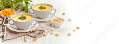 Pumpkin cream soup with croutons  raw fresh pumpkin pieces and herbs on a white rustic wooden background  Autumn concept. Long web format  banner