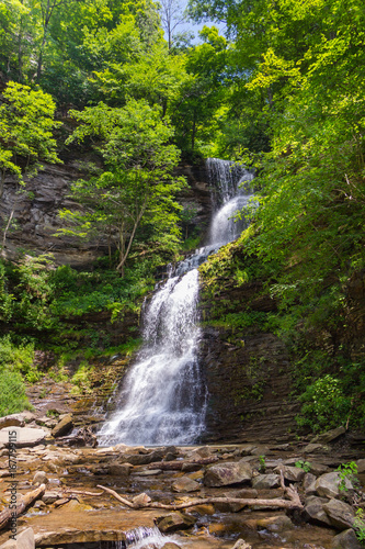 Cathedral Falls in southern West Virginia, a tall beautiful waterfall and stream coming from a rocky outcrop through the sunlit trees of summertime.