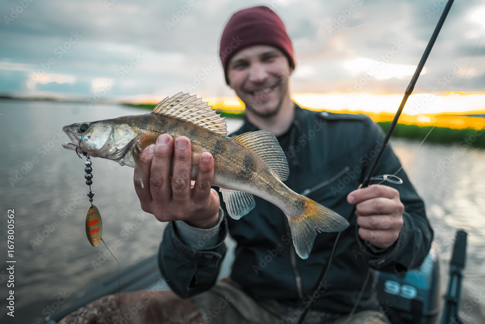 Happy fisherman sits in the boat on the lake and holds the fish Happy fisherman sits in the boat on the lake and holds the fish