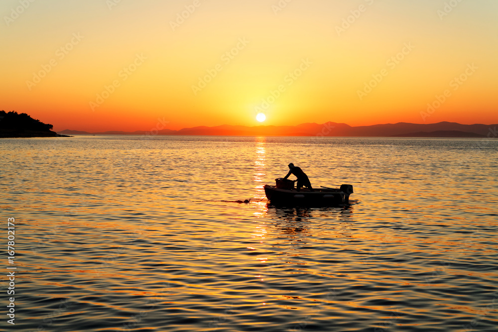 Fisherman in his boat during sunset in a harbor of small town Postira - Croatia
