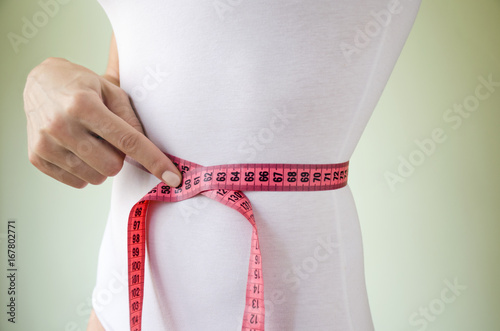 A slender woman in a white underwear with a measuring tape and a hand that points to a thin waist