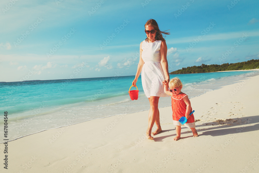 mother and cute little daughter walking on beach