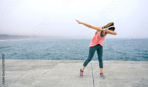 Young woman making dab dance outdoors by sea pier photo