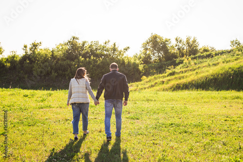 Man and woman holding hands and walking on nature, back view