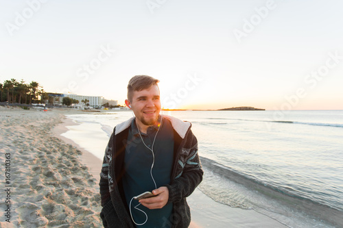Stylish young man listen to music in headphones on a smartphone at the beach. Lifestyle, technology and people concept photo