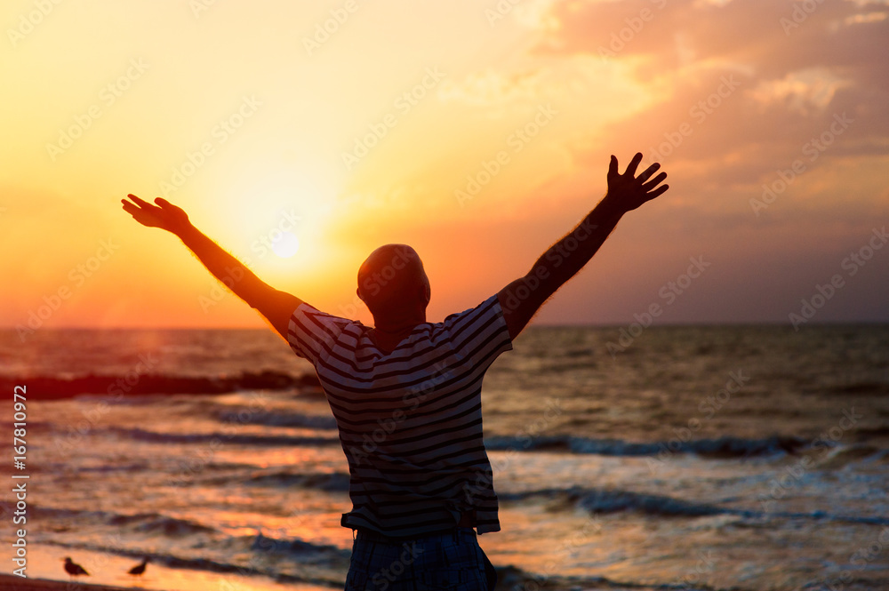 Silhouette of a man raising his hands to the sky at sunset on the beach