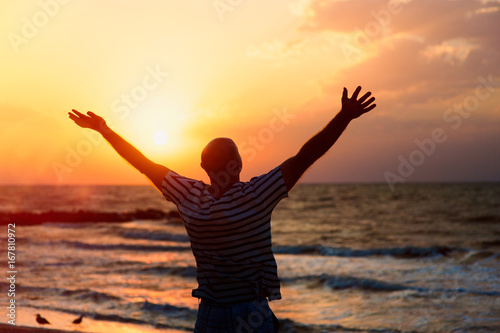 Silhouette of a man raising his hands to the sky at sunset on the beach